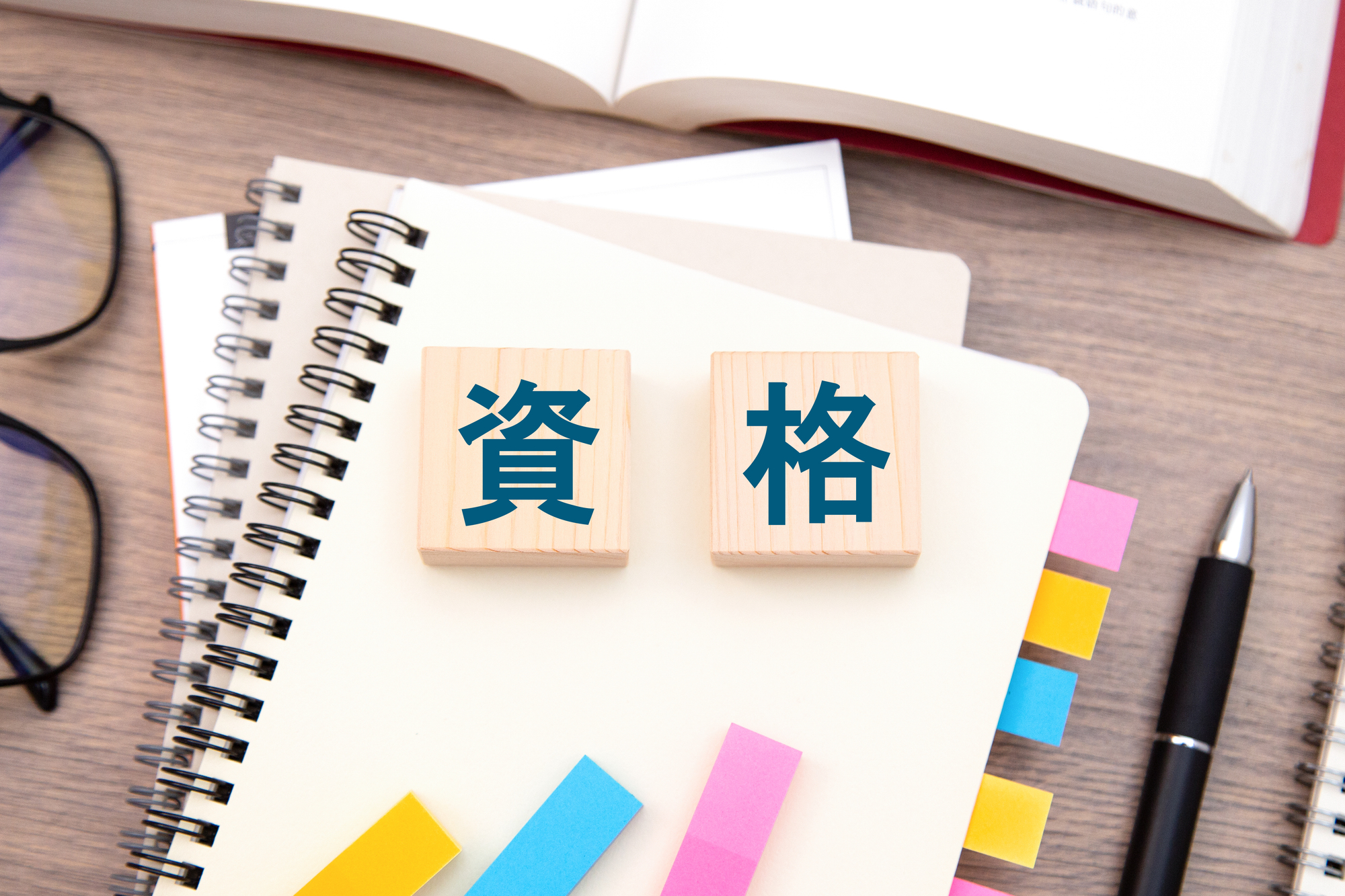 資格と書かれた木製ブロックとノート、付箋、ペン